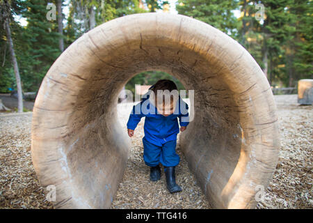 Giovane ragazzo il ducking mentre si cammina attraverso il tunnel nel parco giochi Foto Stock