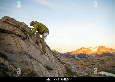 Basso angolo vista del giovane uomo bouldering in Costa montagne, B.C. Foto Stock