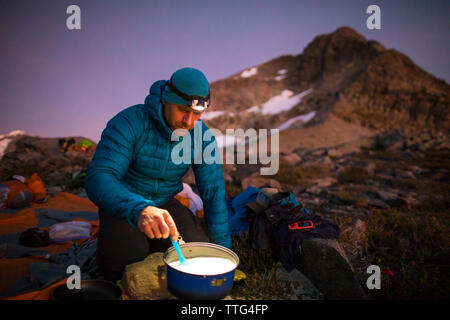 Backpacker cottura su camp stufa e utilizzando il proiettore al tramonto Foto Stock