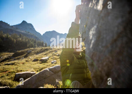 Rocciatore raggiunge per una messa in attesa mentre bouldering all'esterno. Foto Stock