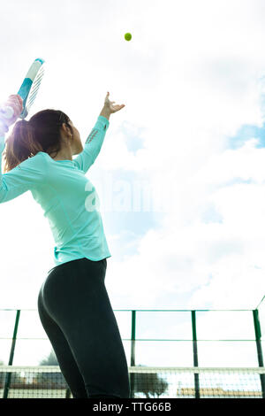 Basso angolo di visione della donna che serve palla da tennis contro il cielo nuvoloso a corte Foto Stock