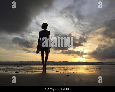 Carefree donna a piedi di spiaggia contro il cielo durante il tramonto Foto Stock