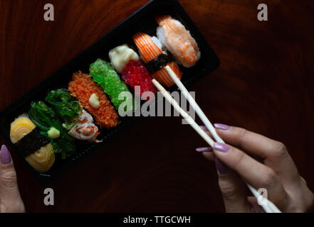 Donna pick un sushi dal vassoio di plastica da bacchette Foto Stock