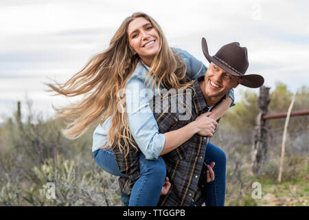 Usura occidentale coppia giovane dando piggy back ride su ranch Foto Stock
