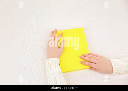 Mani femminili tenendo un libro giallo coperchio sulla scrivania bianca, vista dall'alto Foto Stock