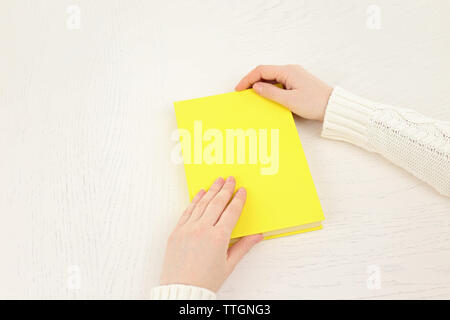 Mani femminili tenendo un libro giallo coperchio sulla scrivania bianca, vista dall'alto Foto Stock