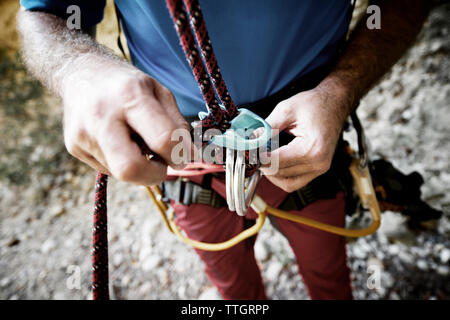 Sezione mediana dei maschi di escursionista regolazione corda di arrampicata in montagna Foto Stock