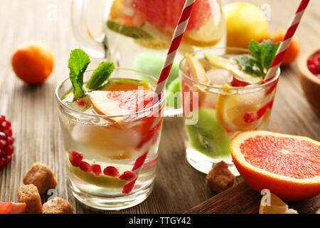 Rinfrescanti cocktail con ghiaccio, menta, i semi di melograno e fette di frutta su sfondo di legno Foto Stock