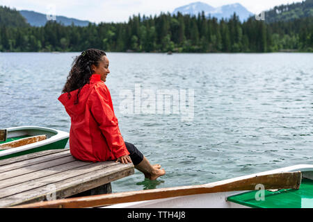 Donna seduta su un pontile e immergendo i suoi piedi in acqua Foto Stock