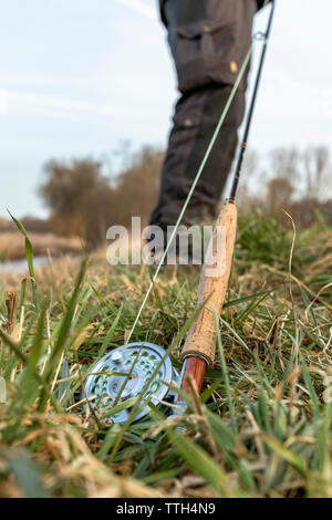 Fisherman prepara il suo fly canna da pesca accanto a un piccolo fiume Foto Stock