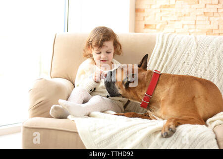 Poco carino ragazza con cane boxer seduto su un divano a casa Foto Stock