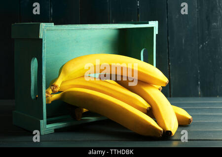 Grappolo di banane mature con scatola in legno scuro dello sfondo Foto Stock