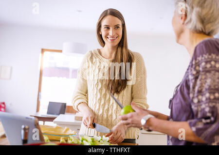 Figlia guardando alla madre durante il lavoro in cucina Foto Stock