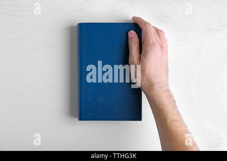 Maschio di tenere in mano il libro blu su bianco tavola. Foto Stock