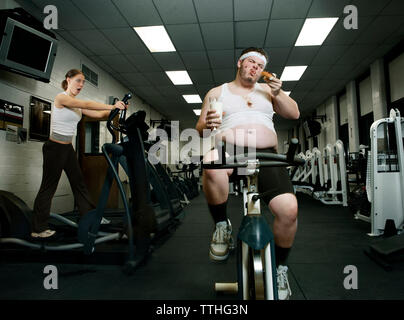 Scioccato donna guardando uomo grasso mangiare ciambella mentre ti alleni in palestra Foto Stock