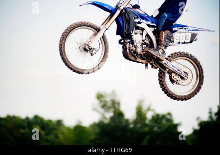 Sezione bassa di biker eseguendo acrobazie a mezz aria contro il cielo chiaro Foto Stock