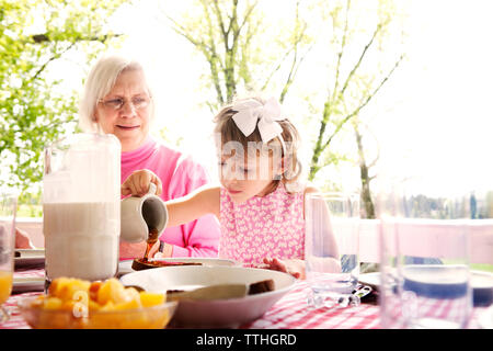 Ragazza di sciroppo di colata sul cibo con la nonna a tavola Foto Stock