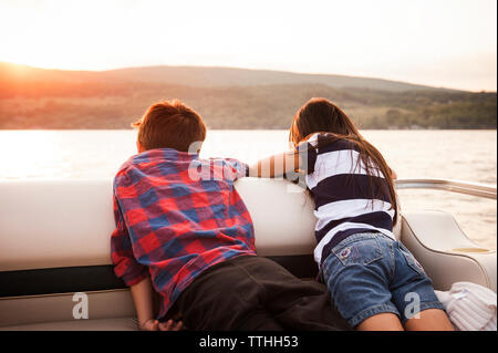Vista posteriore dei fratelli in barca sul lago contro le montagne Foto Stock