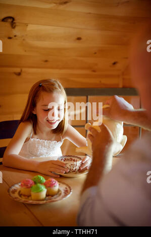 Immagine ritagliata del padre che serve tè al felice figlia durante la seduta a tavola Foto Stock