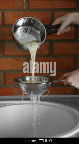 Mani femminili versando acqua dal bollito di spaghetti su lavello in cucina Foto Stock