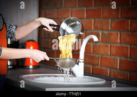 Mani femminili versando acqua dalla pasta bollita su lavello in cucina Foto Stock