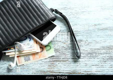 Portafoglio in pelle con il telefono cellulare e le banconote in euro su sfondo di legno Foto Stock