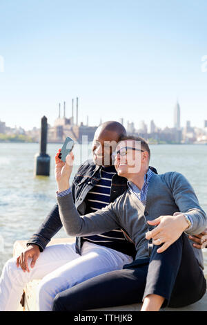 Felice fidanzati tenendo selfie dal fiume contro il cielo chiaro sulla giornata di sole Foto Stock