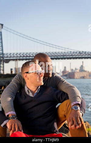 Romantico fidanzati guardando a est del fiume seduti contro il Williamsburg Bridge Foto Stock