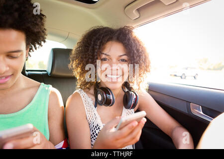 Ritratto di donna usando il telefono mentre è seduto da un amico in auto Foto Stock