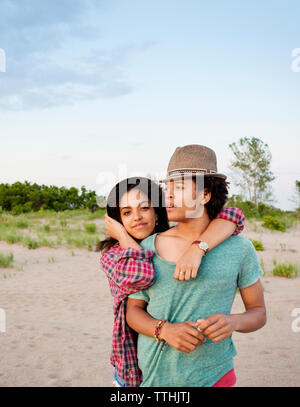 Ritratto di ragazza abbracciando l uomo mentre si sta in piedi in spiaggia contro sky Foto Stock