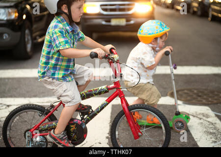 Fratelli push di equitazione scooter e biciclette su strada Foto Stock