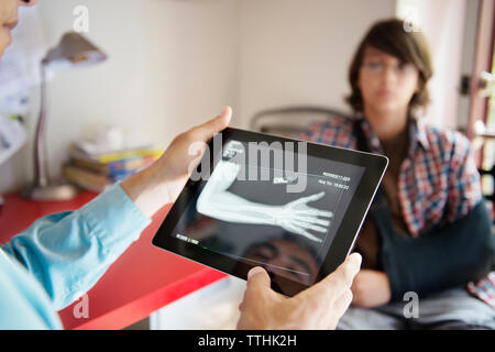 Immagine ritagliata di dottore esaminando la mano X-ray con ragazzo seduto in background Foto Stock