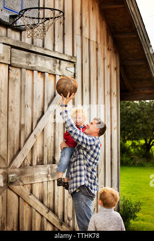 Padre Felice giocando con figli basket granaio esterno Foto Stock