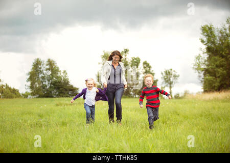 Felice madre a piedi con i bambini sul campo erboso contro sky Foto Stock