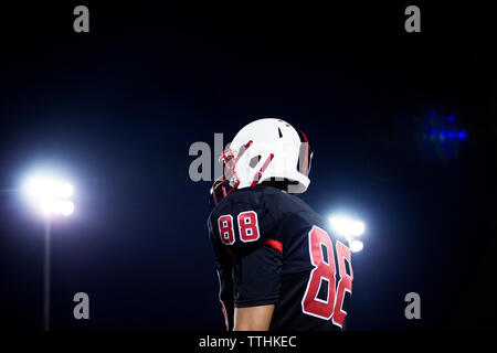 Basso angolo di vista teenage american football giocatori in piedi contro il cielo di notte Foto Stock