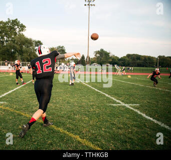 Vista posteriore di adolescenti giocatore di football americano gettando la sfera su campo Foto Stock