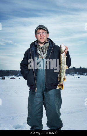 Uomo sorridente tenendo il pesce e in piedi sul lago ghiacciato Foto Stock