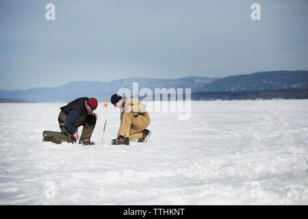 Vista laterale di uomini la pesca sul ghiaccio sul lago ghiacciato contro sky Foto Stock