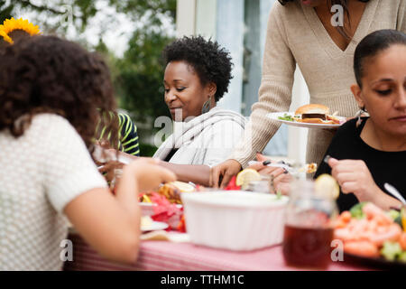 La famiglia e gli amici a mangiare cibo sul tavolo da picnic a backyard Foto Stock