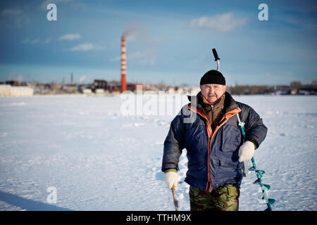 Ritratto di senior uomo che porta trapano mentre si cammina sul lago ghiacciato Foto Stock