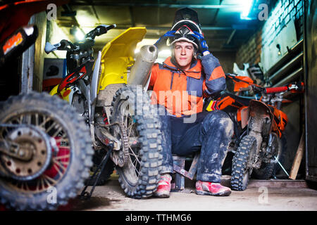 Ritratto di maschio biker holding casco e seduta in garage Foto Stock