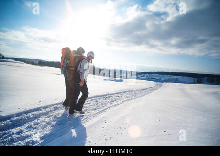 Gli amici che porta uno zaino mentre passeggiate sulla neve campo coperto contro il cielo nuvoloso Foto Stock
