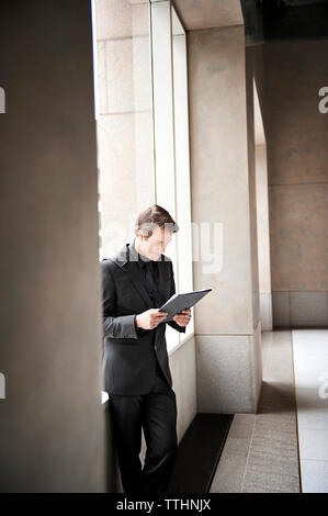 uomo d'affari che legge una cartella mentre si trova in corridoio Foto Stock