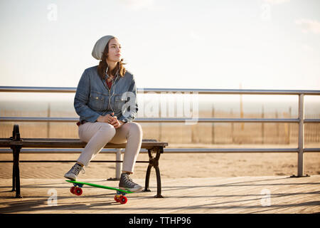 Donna ascoltare musica mentre è seduto sul banco a boardwalk Foto Stock