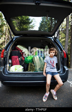 Ritratto di ragazza seduta sul baule auto in strada Foto Stock