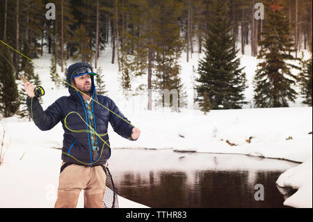 Fly fisherman casting canna da pesca mentre si sta in piedi sul campo nevoso Foto Stock