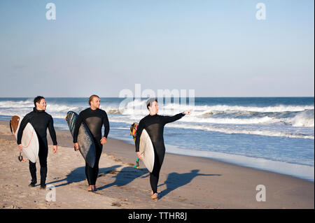 Surfers passeggiate in riva al mare contro il cielo chiaro Foto Stock