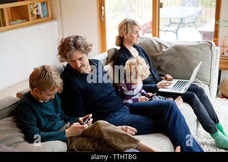 La famiglia tramite laptop e telefono cellulare mentre è seduto sul divano di casa Foto Stock