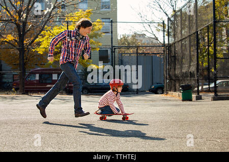 Vista laterale dell'uomo a correre mentre il figlio lo skateboard in posizione di parcheggio Foto Stock