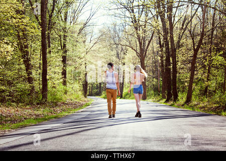 Vista posteriore del giovane camminando sulla strada in mezzo di alberi Foto Stock